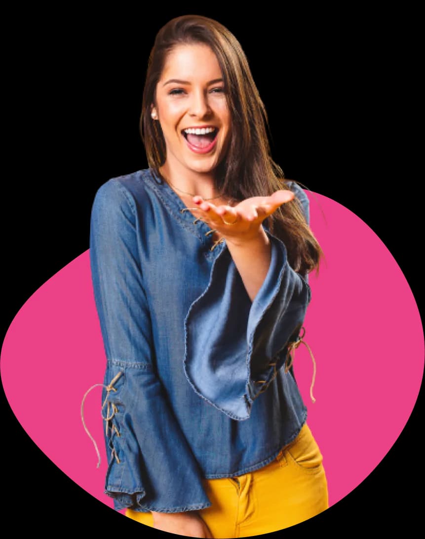 A smiling young woman with long brown hair, wearing a denim top and yellow pants, extending her hand forward as if presenting or inviting
