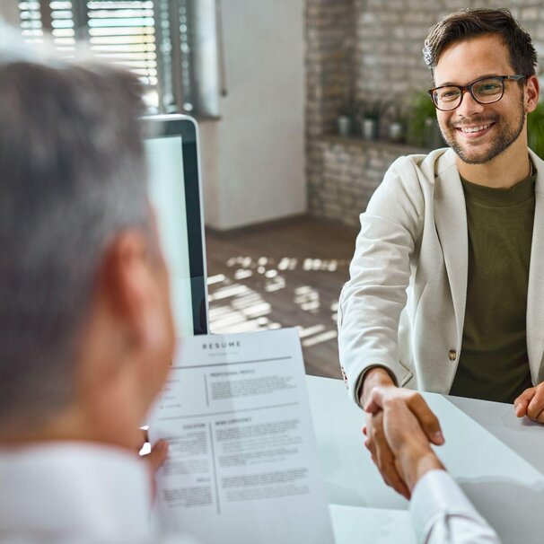Agency owner shaking hands with a new hire across a desk, with a resume on the table